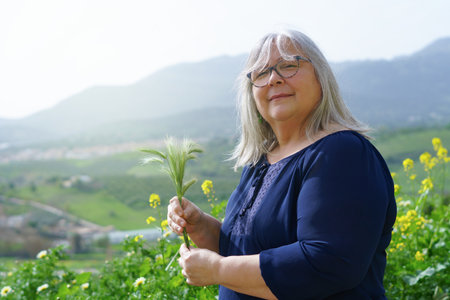 older white-haired woman in the field with ears of barley in her hands with mountain scenery in the...
