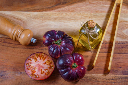 top view of a group of tasty fresh tomatoes of the blue variety next to some wooden tongs, olive oil and a pepper shaker on a wooden table.の写真素材