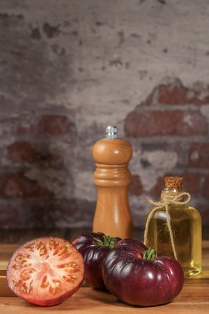 group of tasty fresh tomatoes of the blue variety together with wooden tongs, a glass bottle of olive oil and a pepper shaker on a wooden table.の写真素材