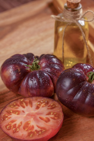 group of blue tomatoes with a tomato cut in half with a bottle of olive oil and some wooden tongs on a wooden tableの写真素材