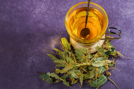 top view glass cup with an infusion of lime blossom tea with fresh leaves around itの写真素材