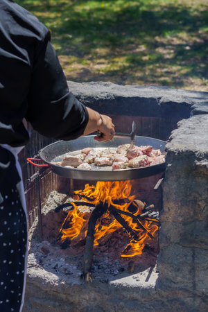woman frying chicken in a paella pan on the fire in the countryside to make a typical spanish paellaの写真素材