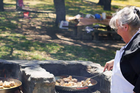 woman cook in a white apron preparing a paella on the fire in the fieldの写真素材