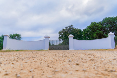 entrance to an agricultural and livestock farm with white walls and a metal gate with a cloudy sky in the background.の写真素材