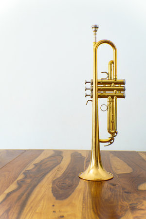 close-up of an old trumpet on a wooden table with a white wall in the backgroundの写真素材