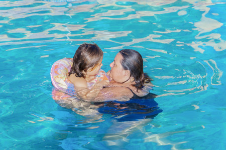 a mother and her young daughter on a float bathing in the pool on a sunny day