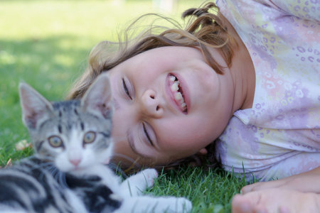pretty long-haired blonde girl lying on the lawn of a garden playing with her little catの写真素材