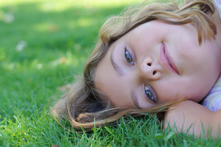 close-up portrait of a pretty blonde girl with long hair and light eyes lying on the lawn of a garden looking at the camera smilingの写真素材