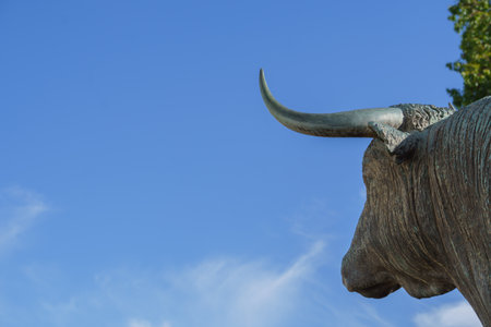bronze sculpture of a bull seen in profile with a blue sky with clouds in the background