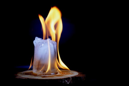ice cube melting in the fire on a wooden disk isolated on a black background