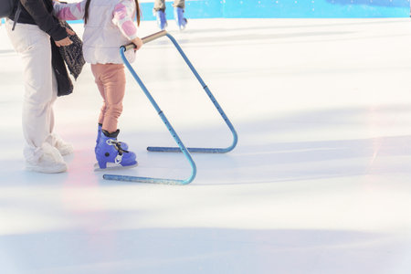girl learning to skate on an ice rink with her motherの写真素材