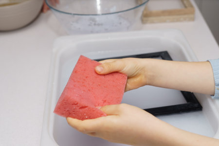 a boy holds a red sponge doing handicraft work at homeの写真素材