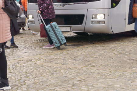 unrecognizable woman traveler getting off a bus with her blue suitcaseの写真素材