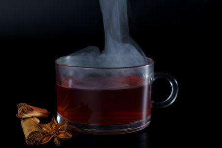 steaming hot cup of red tea with star anise and cinnamon stick, with black background and copy space