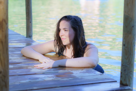 beautiful woman bathing in a lake with her hands folded on a wooden pier looking at the sun.の写真素材