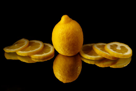 whole lemon with lemon slices on the sides reflected in a mirror with a black backgroundの写真素材