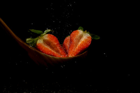 sliced strawberries on a wooden spoon on a black backgroundの写真素材