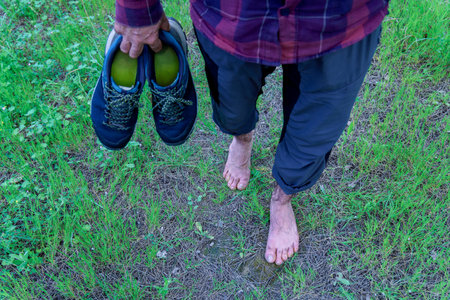 Hiker enjoying walking barefoot on grass holding his trekking shoes in handの写真素材
