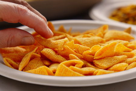 Close-up of a hand grabbing a cheesy puff corn snack from a bowl