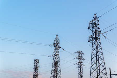 Electricity pylons standing tall against a clear blue sky, symbolizing power distribution and energy infrastructureの写真素材