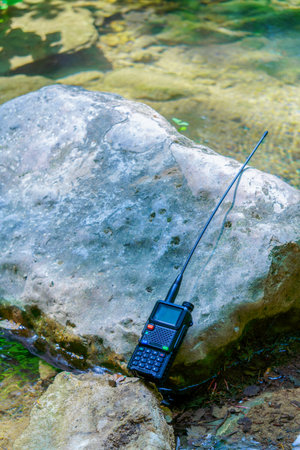 Professional walkie-talkie with long antenna placed on a rock near a water streamの写真素材