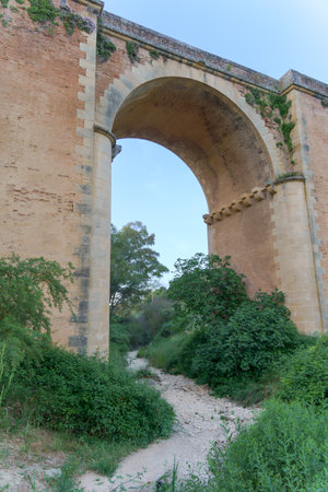 ronda,malaga,spain Dry riverbed with rocks and vegetation passing under an old brick bridge with a large archの写真素材