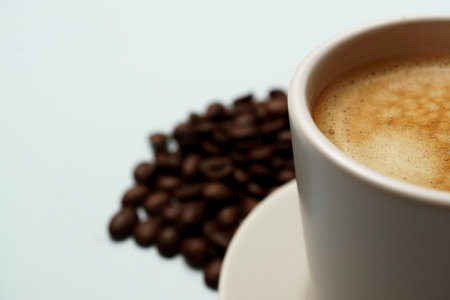 Freshly brewed coffee in a white cup sits on a saucer with roasted coffee beans scattered nearby, creating a cozy and inviting sceneの写真素材