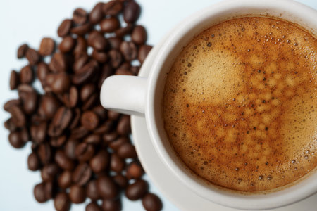 Freshly brewed coffee with crema in a white cup, accompanied by roasted coffee beans, creating a cozy and inviting sceneの写真素材