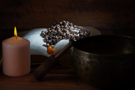 Tibetan singing bowl, rosary beads, and a lit candle create a peaceful atmosphere on a wooden surfaceの写真素材