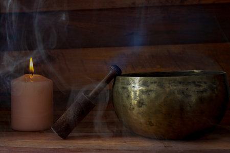 Tibetan singing bowl, candle and mallet on wooden surface with smoke, creating a spiritual atmosphereの写真素材