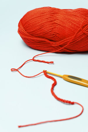 Red yarn and a crochet hook creating a chain stitch on a white backgroundの写真素材