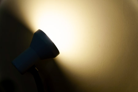 Light beam from a desk lamp illuminates wall, creating warm light and shadowsの写真素材