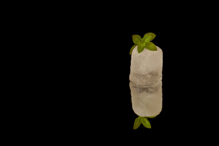 Ice cube with mint leaves reflecting on a black background, creating a refreshing and minimalist imageの写真素材