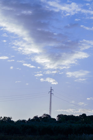 Metal electricity pylon transporting energy through wires, set against a backdrop of a cloudy sunset skyの写真素材