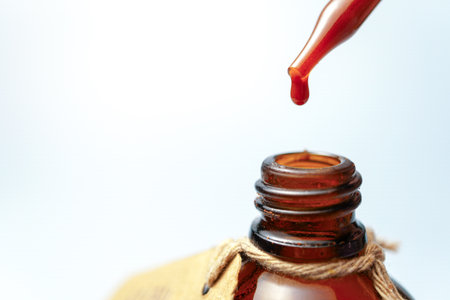 Red liquid dripping from a pipette into an amber bottle, creating a visually appealing contrast against a light backgroundの写真素材