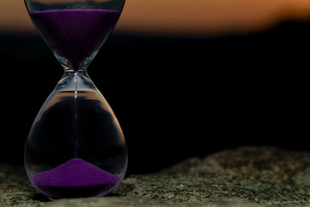 Purple sand hourglass is measuring passing time during sunset on rock surfaceの写真素材