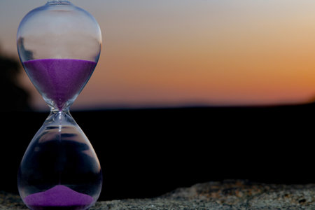 Purple sand hourglass is showing the passage of time against a beautiful sunsetの写真素材