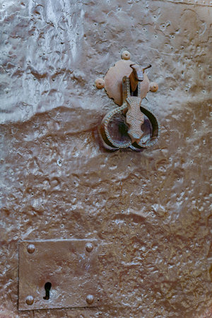 Close-up of an old weathered metal door featuring a distinctive bull-shaped handle, highlighting the...