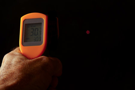 Hand using an infrared thermometer showing 30.9 degrees celsius on a black background