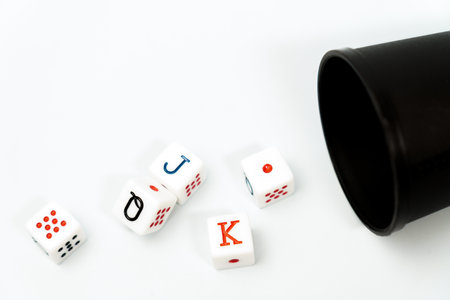 Poker dice spilling from a black dice cup onto a white background, representing gambling and games...