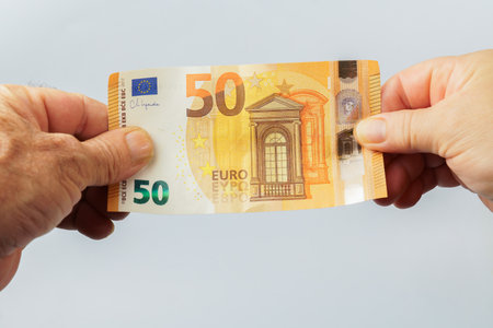 Two hands holding a slightly folded fifty euro banknote on a white background