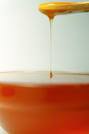 Honey pouring from wooden spoon into bowl, creating splash and ripplesの写真素材