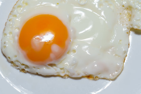 Close-up of a single fried egg sunny side up, showing the golden yolk and crispy edges of the egg...