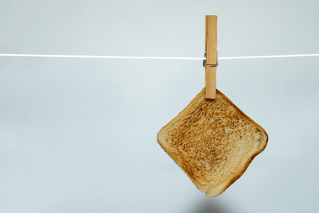 Toasted bread hanging on clothesline with clothespin against white backgroundの写真素材