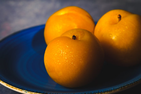 Bright yellow plums on a blue plate, featuring refreshing water drops