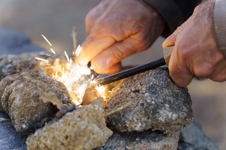 Bushcraft survivalist creating fire sparks with a ferro rod and cotton tinder, gathering heat...
