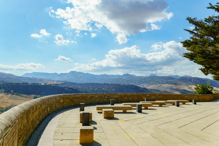 Ronda viewpoint terrace offers stone benches for relaxing while observing the scenic mountain landscape under a bright sky in Ronda, Malaga, Spainの写真素材