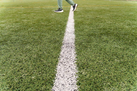 Person walking across a white line on a green artificial turf soccer field, representing progress or...