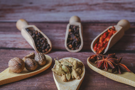 Various whole spices and dried chili peppers are artfully arranged on wooden spoons, creating an aromatic cooking ingredient collectionの写真素材