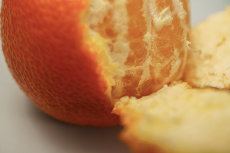 Orange fruit partially peeled close-up revealing its vibrant orange pulp, segments, and white pith, highlighting healthy eatingの写真素材